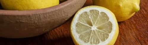 whole lemon in clay bowl. whole and half lemon outside of bowl on wooden table